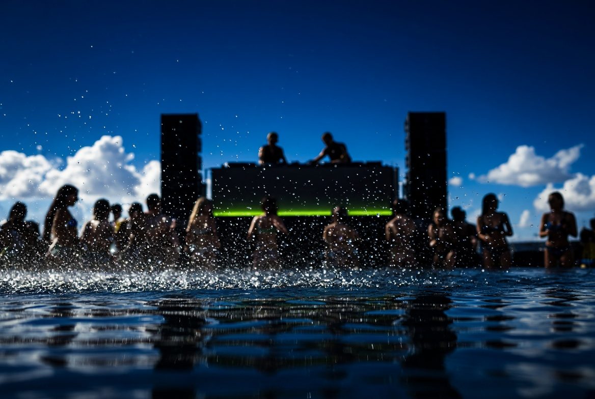 Daytime pool party DJ booth viewed across the water